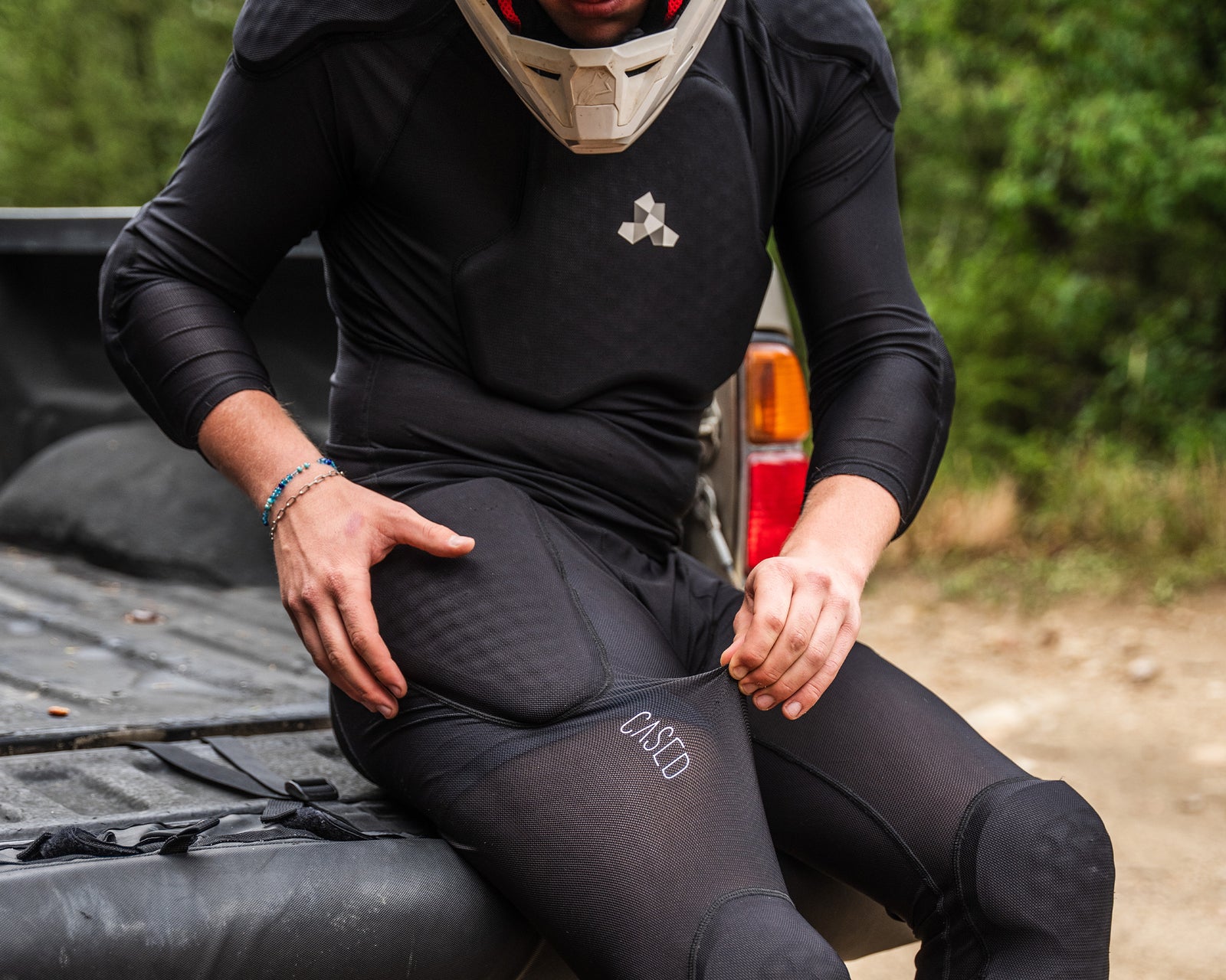 A moto rider sitting in the bed of a pick-up truck showing the elasticity and flexibility of Cased inner-protective pants.