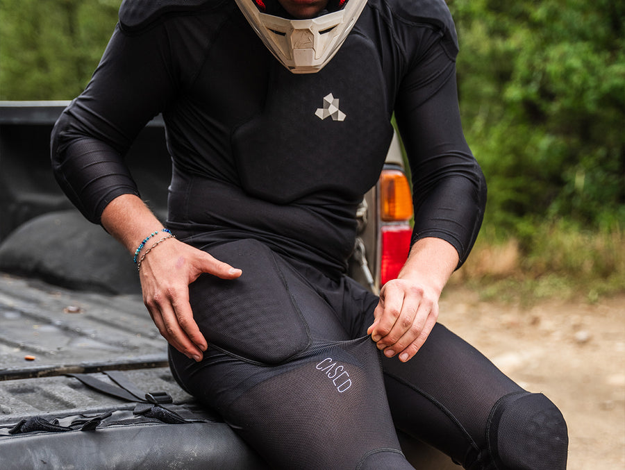 A moto rider sitting in the bed of a pick-up truck showing the elasticity and flexibility of Cased inner-protective pants.